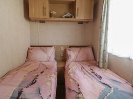 A bedroom with two single beds with pink patterned bedding and a wooden cabinet above at Ashcroft in Warton Lancashire