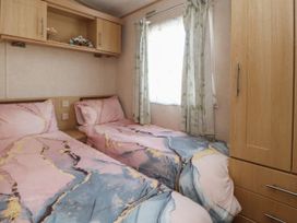 A bedroom with two single beds with patterned bedding a window with curtains and wooden storage units at Ashcroft in Warton Lancashire