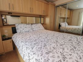A bedroom with a bed covered in leaf patterned bedding wooden cabinets and mirrored wardrobes at Ashcroft in Warton Lancashire