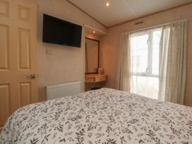 A bedroom with a bed covered in leaf patterned bedding a wall mounted TV a dressing table with mirror and a window with curtains at Ashcroft in Warton Lancashire