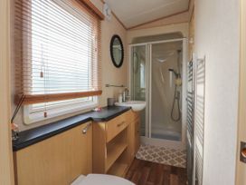 A bathroom with a shower enclosure sink toilet wooden cabinets and a window with blinds at Ashcroft in Warton Lancashire