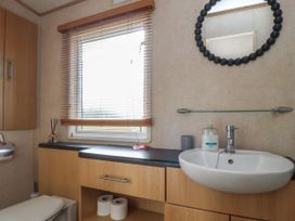 A bathroom with a toilet a sink with soap a round mirror wooden cabinets and window blinds at Ashcroft in Warton Lancashire