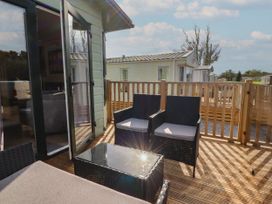 An outdoor wooden deck with two cushioned chairs and a glass-top table adjacent to a light green building at Ashcroft in Warton Lancashire