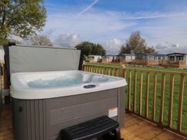 An outdoor hot tub on a wooden deck overlooking a grassy area with several mobile homes in the background at Ashcroft in Warton Lancashire