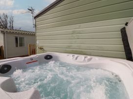 A bubbling outdoor hot tub beside a green siding wall and a neighboring beige building at Ashcroft in Warton Lancashire
