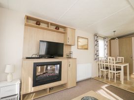 A living room with a television above a fireplace and a dining table with chairs near a window at 610 Caravan in Bognor Regis