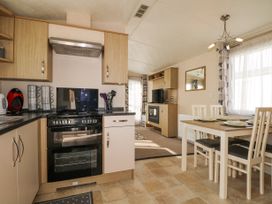 A kitchen with stove and dining table with plates next to a living room with tv and fireplace at 610 Caravan in Bognor Regis