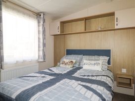 A bedroom with a bed next to a window and wooden overhead cabinets at 610 Caravan in Bognor Regis