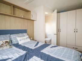A bedroom with a bed partially covered with blue and white bedding a wall shelf a small cabinet a partially open door showing a toilet and a wardrobe at 610 Caravan in Bognor Regis