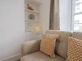 A beige sofa with textured cushions next to a built-in shelf with nautical decorations and a window with curtains at 47 Church Street in Lyme Regis