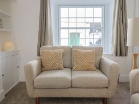 A beige loveseat with two textured cushions in front of a window with curtains and a lamp on the side at 47 Church Street in Lyme Regis
