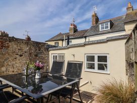 An outdoor patio area with a glass table and black chairs with flowers and wine glasses at 47 Church Street in Lyme Regis
