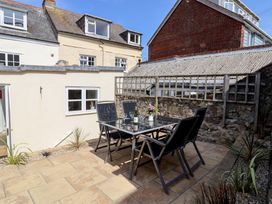 An outdoor patio with a glass table and four chairs next to a stone wall at 47 Church Street in Lyme Regis