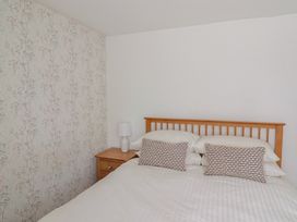 A bedroom with a wooden bed frame white bedding two patterned pillows a wooden nightstand and a white lamp at 47 Church Street in Lyme Regis