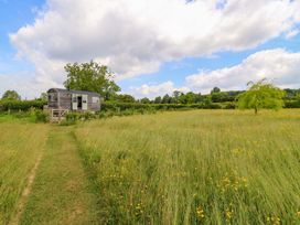 An outdoor area with a shepherd hut surrounded by grass and wildflowers at Goose Whistle Hut in Foxham