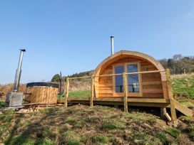 A wooden pod with a deck and railing next to a hot tub on a grassy hill at Holbein in Matlock