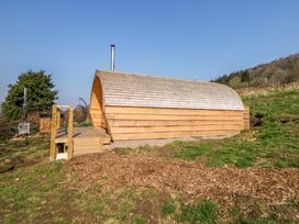 A wooden cabin with a curved roof and a small deck in a grassy rural area at Holbein in Matlock