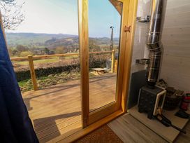 A wood burning stove next to a glass door opening to a wooden deck with a view of hills at Holbein in Matlock