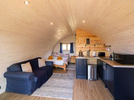 An open plan cabin interior with a blue sofa a bed with floral bedding and a kitchenette at Holbein in Matlock