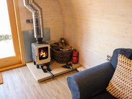 A wood stove with fire burning next to a basket of firewood and a fire extinguisher in a room with wooden walls and floor at Holbein in Matlock