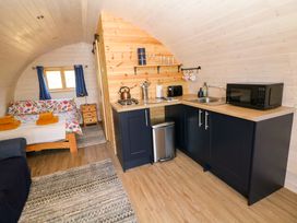 A small room with a bed with floral bedding a kitchenette with black cabinets a microwave a sink and a stove at Holbein in Matlock