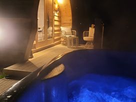 A wooden deck with two chairs and a table outside a cabin with a hot tub in the foreground at Holbein Matlock