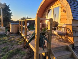 A wooden cabin with a small deck with two chairs and a hot tub outside surrounded by grass at Holbein in Matlock