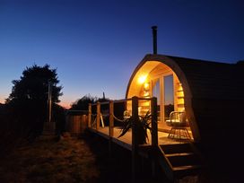 A wooden pod with lit porch lights and chairs on a deck at Holbein in Matlock