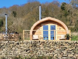 A wooden pod with a curved roof and glass doors with chairs on a small porch behind a stone wall at Holbein in Matlock