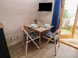 A dining area with a wooden table set for two with bowls plates glasses and cutlery two cushioned chairs a wall mounted television blue curtains and an open door to a deck at Holbein in Matlock