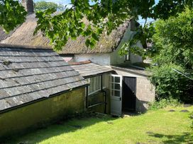 A garden view of a stone building with a thatched roof at Vinney Cottage in Owermoigne