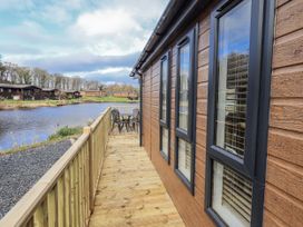 An outdoor deck with a table and chairs overlooking a lake at Lakeside Lodge Bowland Lakes Leisure Village near Garstang