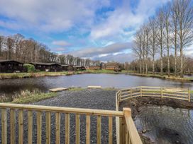 View of a pond with log cabins and trees at Lakeside Lodge Bowland Lakes Leisure Village near Garstang