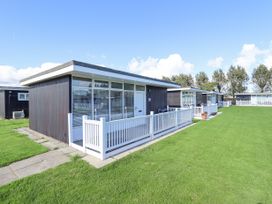 A group of modern single storey holiday chalets with white fences and green lawns at 104 The Laurels in Chapel St Leonards