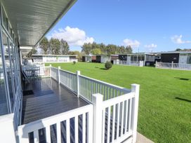 Decking area with white railing and adjacent grass lawn with small trees at 104 The Laurels in Chapel St Leonards