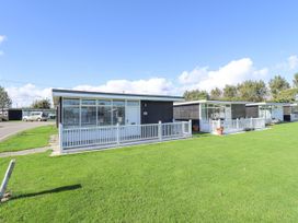 Small black and white holiday chalets with fenced patios on a grassy lawn at 104 The Laurels in Chapel St Leonards