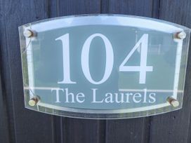 A house number sign reading 104 The Laurels on a dark wooden wall at 104 The Laurels in Chapel St Leonards