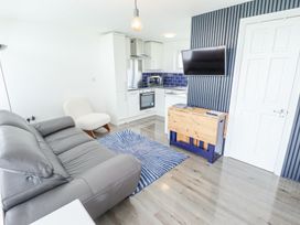 A living area with grey sofa white chair blue and white rug wall mounted tv and small kitchen at 104 The Laurels in Chapel St Leonards