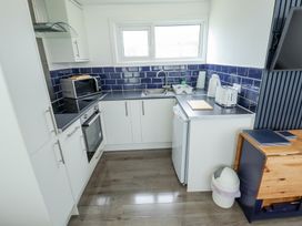 A kitchen with white cabinets a microwave oven a sink a kettle a toaster a small refrigerator and a trash bin at 104 The Laurels in Chapel St Leonards