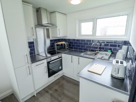 A kitchen with white cabinets blue tiled backsplash oven microwave sink and toaster at 104 The Laurels in Chapel St Leonards