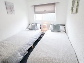 A bedroom with two single beds a window with a blind and a nightstand with a lamp between the beds at 104 The Laurels in Chapel St Leonards