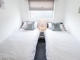 A bedroom with two single beds separated by a nightstand with a lamp at 104 The Laurels in Chapel St Leonards