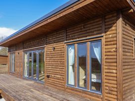 The exterior of a wooden cabin with large windows and a door opening onto a wooden deck at Foxglove in Higher Wambrook near Chard