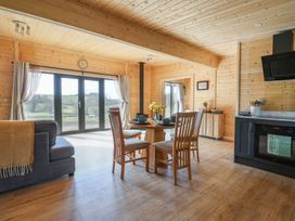 An open dining and kitchen area with wooden walls and ceiling a round dining table with four chairs a grey sofa and large glass door with curtains at Foxglove Higher Wambrook near Chard