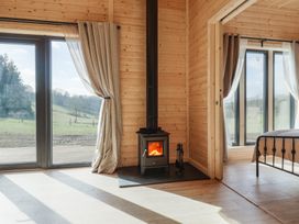 A wood paneled room with a wood burning stove near large glass doors and a bedroom visible through an open doorway at Foxglove Higher Wambrook near Chard