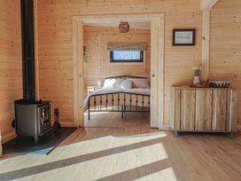 A wooden room with a black wood stove on the left and a wooden cabinet on the right with a bedroom visible through a doorway at Foxglove in Higher Wambrook near Chard