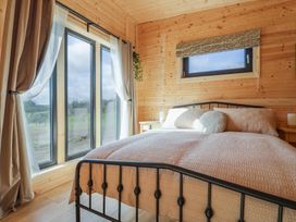A bedroom with a metal bed frame a window with curtains and wooden walls at Foxglove in Higher Wambrook near Chard