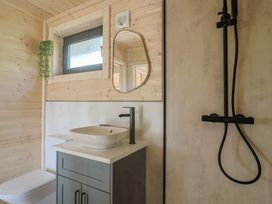 A bathroom with a toilet, sink with cabinet, mirror, shower area, and a window at Foxglove Higher Wambrook near Chard