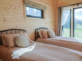 A bedroom with two single beds having pink bedding and round cushions with window and sliding glass door showing outdoor view at Foxglove in Higher Wambrook near Chard