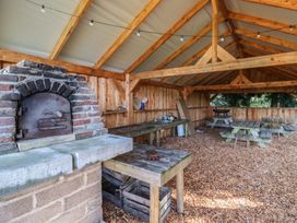 An outdoor covered area with wooden tables a brick oven and string lights at Foxglove in Higher Wambrook near Chard